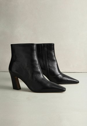 Black leather ankle boots with a pointed toe, textured finish, and a block heel. Side zipper detail. Smooth surface and sleek design.