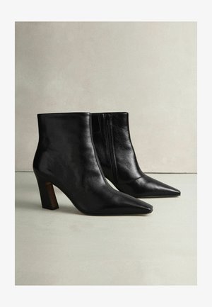 Black leather ankle boots with a pointed toe, textured finish, and a block heel. Side zipper detail. Smooth surface and sleek design.