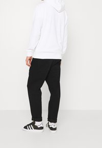 Sudadera blanca con bolsillo canguro, pantalones jogger negros ajustados y zapatillas Adidas en blanco y negro. Texturas suaves de algodón y denim visibles.