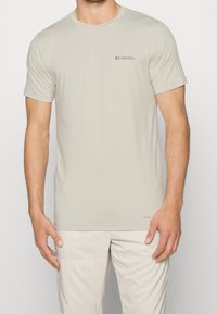 Světlobéžové tričko s krátkým rukávem, vyrobené z měkké látky, s kulatým výstřihem a malým logem Columbia na levé straně hrudi.