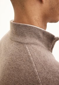Pullover beige lavorato a maglia con colletto alto, caratterizzato da una finitura testurizzata e un collo a coste. Vista laterale che mostra i dettagli delle cuciture e della vestibilità.
