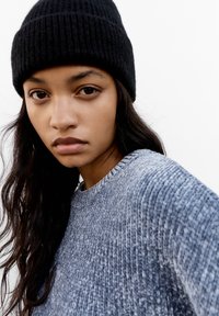 Pull en mailles texturé bleu clair avec un bonnet noir côtelé, présentant un col rond et des motifs de tricot visibles, sur fond blanc.