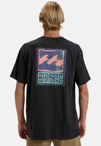 Must musta särk, millel on lühikesed varrukad ja seljal värvikas lainegraafika, kus on silmatorkav "BILLABONG" tekst ja detailne äärise disain.