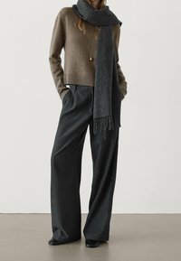 Maglione marrone corto con orlo a coste, abbinato a pantaloni grigi a righe larghe. Un foulard grigio scuro con frange completa il look.