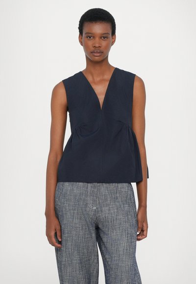 Top senza maniche di colore navy con scollatura a V profonda, caratterizzato da dettagli arricciati in vita e una silhouette strutturata. Abbinato a pantaloni grigi testurizzati.