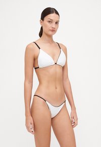 Ensemble de bikini blanc comprenant un haut triangulaire avec des bretelles noires et une fine bande contrastante. Le bas est également minimal avec une taille basse.