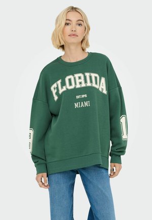 Green sweatshirt with "FLORIDA" and "MIAMI" printed in white, featuring oversized fit, long sleeves, and ribbed cuffs. Worn with blue jeans.