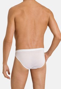 Bílé bavlněné kalhotky s hladkým povrchem a elastickým páskem, zobrazené zezadu na holém trupu s přirozeným tónem pleti.