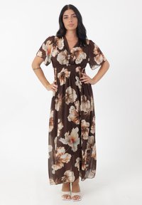 Robe maxi florale marron avec de courtes manches bouffantes, taille smockée et grands motifs de fleurs beige et pêche. Tissu léger et fluide avec une texture douce.