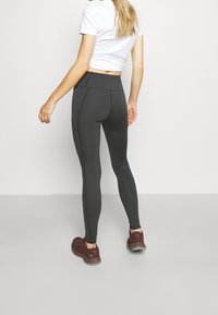 Leggings noires avec une taille haute, présentant des coutures contrastées et un design ajusté, associées à un t-shirt court blanc et des chaussures bordeaux.