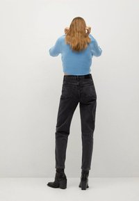 Pull en tricot bleu, crop, jeans en denim noir taille haute et bottines noires à talons, vus de dos sur un fond neutre.