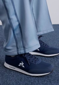 Marinblå sneakers med vit sula och logotyp, kombinerade med ljusblå träningsbyxor med mörkblå sidostripes och en mjuk tygtextur.