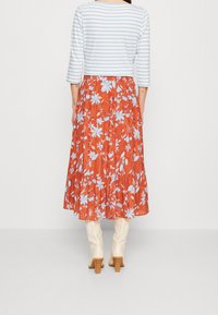 Gestreiftes hellblaues Crop-Top mit dreiviertel Ärmeln kombiniert mit einem fließenden orangen, floralen Maxiskirt, der mit blau-weißen Blumen verziert ist.