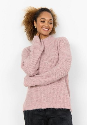 Rosa stickad tröja med hög krage, ribbad textur, långa ärmar och avslappnad passform, bärs över mörka mönstrade byxor.