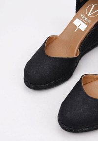 Zapatos de cuña de lona negra con puntera descubierta, plantilla de cuero marrón y suela de plataforma de yute trenzado. Presentan costuras mínimas y un tejido texturizado.