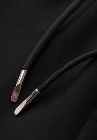 Deux cordons de capuche noirs avec embouts métalliques posés sur un tissu noir en gros plan.