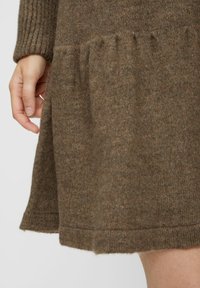 Bruine gebreide jurk met een geribbelde mouw en een gelaagde ruchesrand. Zachte textuur met subtiele kleurvariaties.