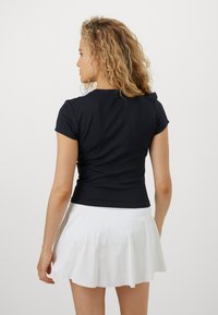 Haut ajusté à manches courtes de couleur noire avec un col rond, porté avec une jupe évasée blanche. Le tissu semble lisse et élastique, offrant un confort optimal.