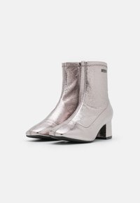 Botas de tobillo metálicas rosas con punta afilada, cierre de cremallera y un tacón bajo. Textura suave con detalles de costura visibles.