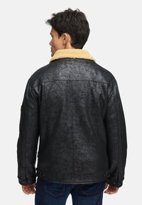 Schwarze Lederjacke mit strukturierter Oberfläche, ausgestattet mit einem beigen, künstlichen Schafslederkragen und Knopfdetails an den Bündchen.