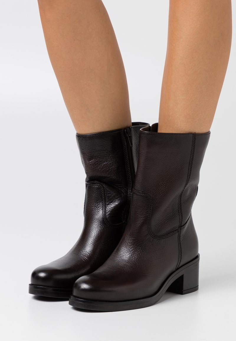 Bottes en cuir noir mi-mollet à talons blocs portées sur jambes nues, avec fermetures éclair latérales et bouts arrondis.