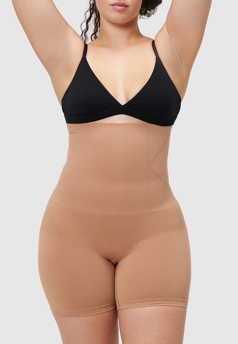 Beżowy, wysoki pas gorsetu modelującego wykonany z gładkiej, elastycznej tkaniny. Posiada bezszwową konstrukcję z cięciem na wysokości środkowej części uda i bez widocznych zapięć.