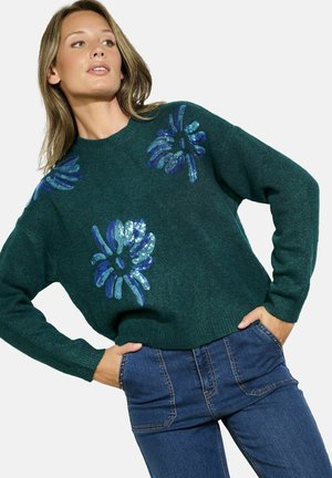 Groene gebreide trui met blauwe sequins bloemenpatronen, voorzien van een ronde hals en lange mouwen, gecombineerd met hoge taille blauwe jeans.
