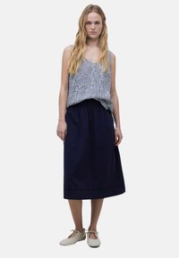 Topped sin mangas con un patrón en azul y blanco, combinado con una falda navy oscura. El conjunto incluye unos zapatos planos de color claro con cintas.
