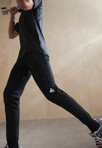 Melnas sporta bikses ar pieguļošu piegriezumu, ar baltu logotipu uz kreisās kājas. Materiāls izskatās viegls un elastīgs, piemērots treniņiem.