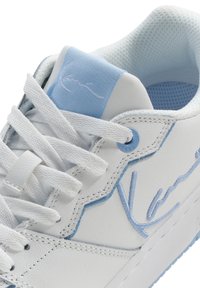 Witte sneaker met lichtblauwe accenten, leren textuur en geborduurd logo. Beschikt over platte veters en een gevoerde inlegzool.