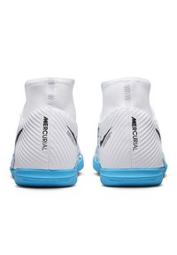 Valkoiset jalkapallon nappulakengät, joissa on uurrettu pinta, korkea nilkka, sininen pohja ja mustat logoakenniset. Varustettu ei-jättävällä kumipohjalla pidon parantamiseksi.