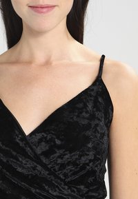 Black velvet dress with a wrap design, featuring thin straps and a soft, textured fabric that shines in light, highlighting its deep color.