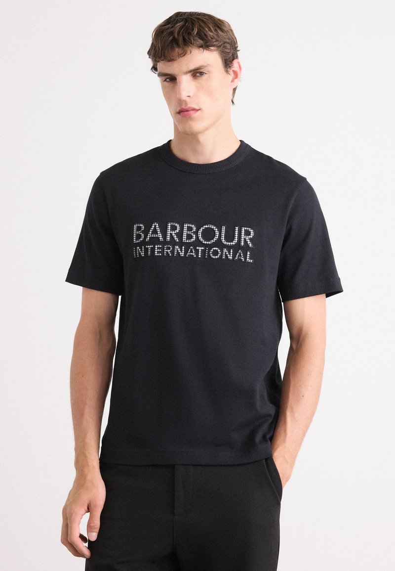 T-shirt de algodão preto com mangas curtas, decote redondo e logotipo "BARBOUR INTERNATIONAL" em fonte branca texturizada na frente.