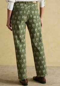 Zelené nohavice s kvetinovým vzorom a rovný strihom, ktoré majú zadné vrecká a textúrovanú látku. Hnedé topánky dopĺňajú outfit.