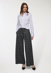 Camicia bianca con bottoni e maniche lunghe, abbinata a pantaloni a gamba larga e vita alta in tartan scuro. Tacchi a punta neri.