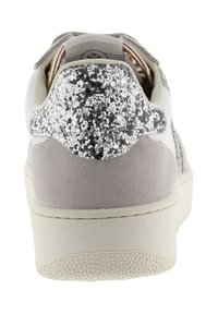 Sneaker bianca e grigio chiaro vista da dietro, con un dettaglio al tallone in argento e nero glitterato e una suola testurizzata color avorio.