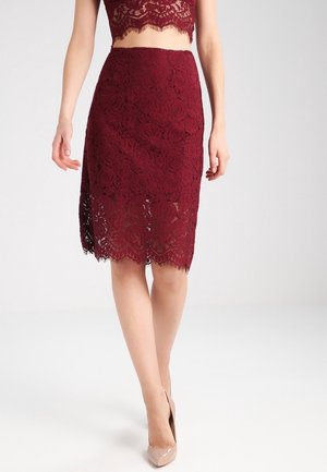 Bordowa ołówkowa spódnica z koronki z kwiatowym wzorem, falbankowym brzegiem i dopasowanym krojem, zestawiona z beżowymi szpilkami.