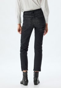Vaqueros skinny de denim negro con cintura alta, que cuentan con un diseño clásico de cinco bolsillos y detalles de costura sutiles. Llevados con botas de tobillo.
