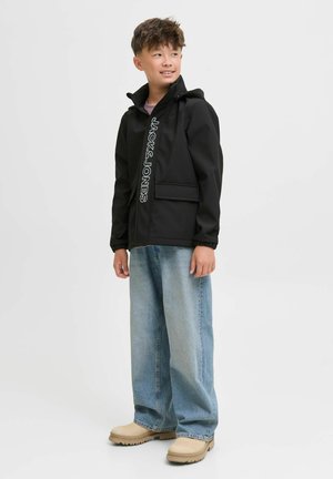 Svart zip-jacka med huva och frontfickor, med vit text "JACK & JONES". Matchad med ljusblå baggy jeans och beige skor.