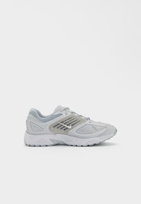 Light gray athletic shoe with a mesh upper, padded collar, subtle stripes, and a rubber sole. Features branding on the side and laces.