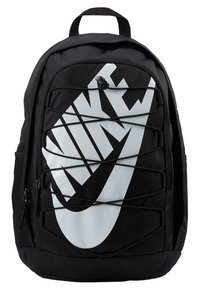 Black fabric backpack featuring a large white Nike logo, elastic bungee cord design on the front, and zippered pockets on sides.