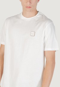 T-shirt bianca in cotone. Caratterizzata da un collo rotondo e maniche corte, con una piccola etichetta di marca sul lato sinistro. Texture liscia.