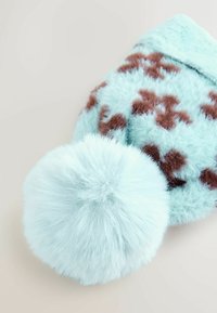 Gorro de piel sintética en azul claro con patrón de estrellas marrón; cuenta con un gran pompón esponjoso en la parte superior. Tejido suave y texturizado.