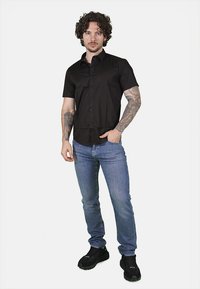 Camicia nera a maniche corte con bottoni, aderente, abbinata a jeans azzurri e sneaker sportive nere. Tessuto liscio e uniforme.