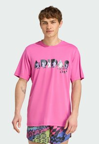 Kortærmet lyserød t-shirt med "ADIDAS" logo i sort og hvid, prydet med legende karaktergrafikker. Glat stof med en afslappet pasform.