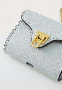 Accessorio in pelle testurizzata di colore azzurro chiaro con hardware dorato e chiusura a patta. Presenta un'apertura a forma di ritaglio per l'accesso; i bordi sono rifiniti in marrone.