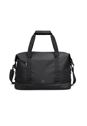 Schwarze rechteckige Reisetasche mit zwei Griffen, Schulterriemen und kleinem Aufnäher mit rot-weißen und blauen Streifen auf der linken Seite.