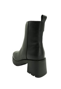 Bota de cuero negro hasta el tobillo con tacón bloque robusto, tirador en la parte posterior y suela estriada para mayor agarre, mostrada desde un ángulo lateral trasero.