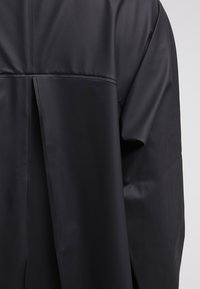 Svart, vattentät jacka med slät yta, lös passform och bakre ventilationsspringa med minimalistisk design.