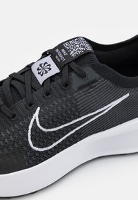 Sort løbesko med en tekstureret overdel, hvidt Swoosh-logo og en sort label med QR-kode. Gummisål og snørelukning.